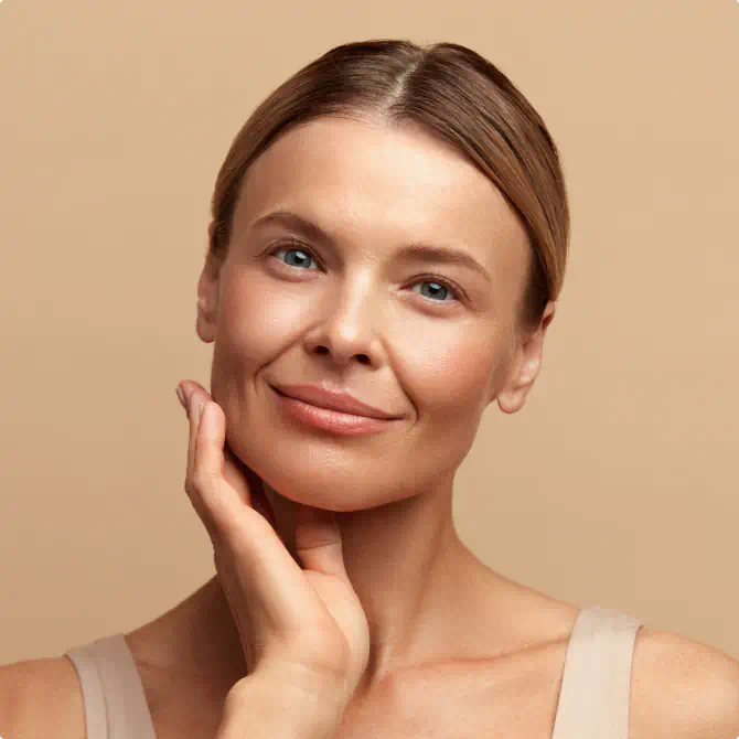 Woman with a radiant complexion touching her face against a beige background