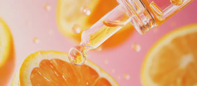 Glass dropper with vitamin C serum above fresh orange slices