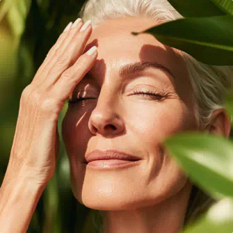 A close-up of a woman with light skin and gray hair, gently touching her forehead
