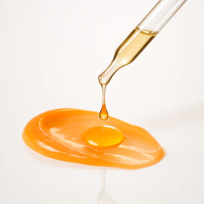 Dropper releasing oil onto a glossy orange skincare gel