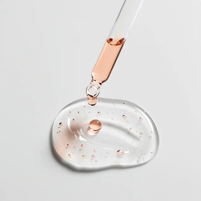 Dropper releasing a clear, slightly pink serum